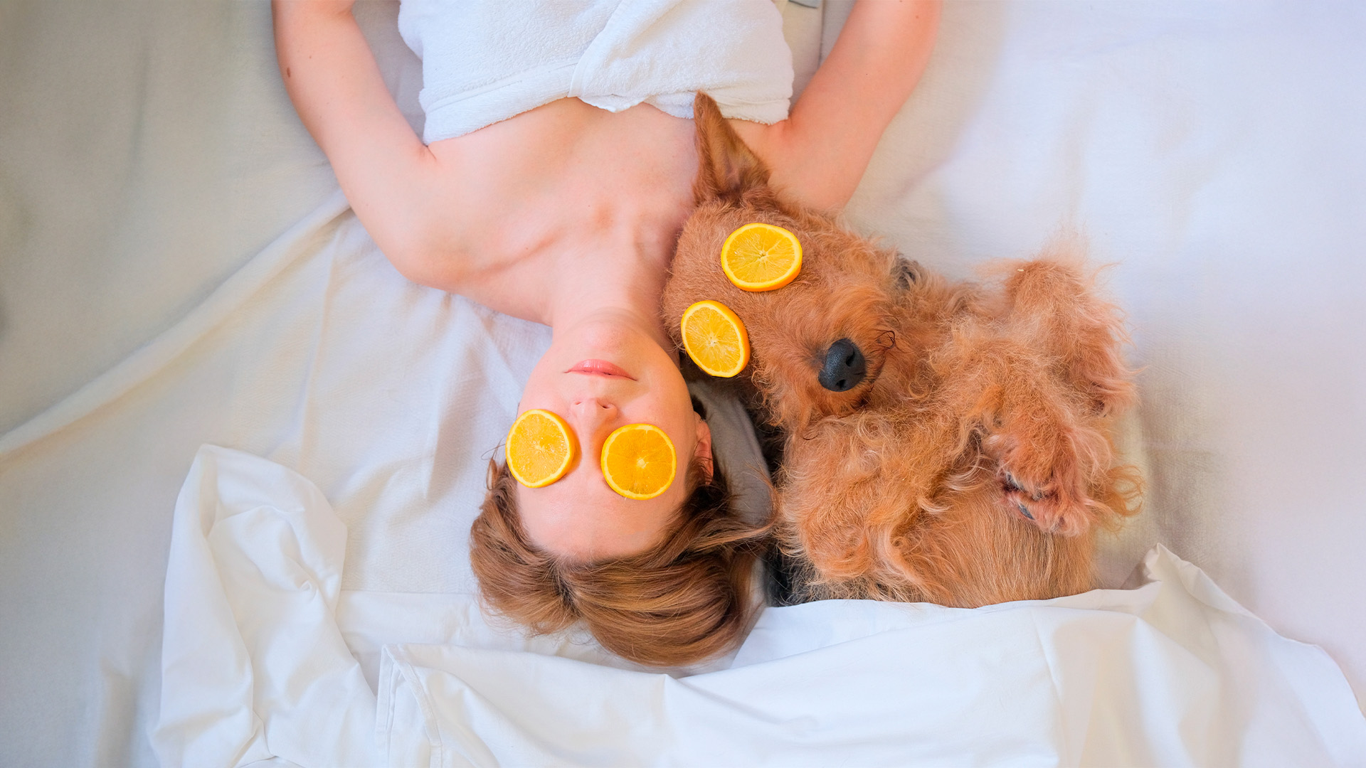 woman and dog laying in bed with orange slices covering their eyes